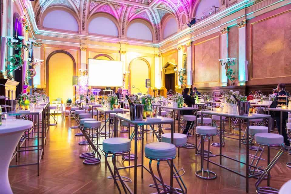 Elegantes Hochzeitslocation in einem prachtvollen Saal mit farbiger Beleuchtung und festlich gedeckten Tischen.