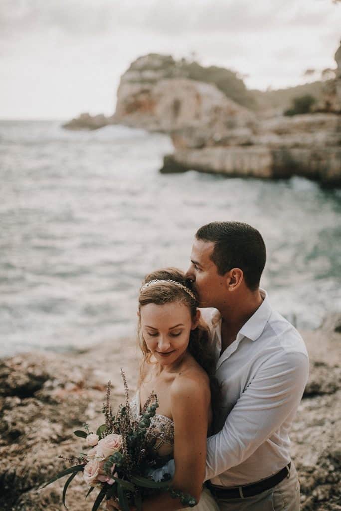 Romantisches Hochzeitsfoto am Strand mit verliebtem Paar und Blick auf die Küstenklippen in Tirol, Österreich.