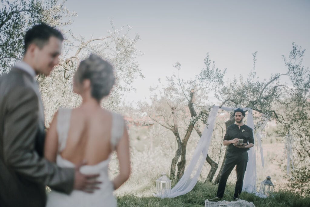 Liebevolles Hochzeitsfoto bei Outdoor-Zeremonie in Tirol, Braut und Bräutigam, Fotograf im Einsatz, romantische Kulisse mit Bäumen und Dekorationen.
