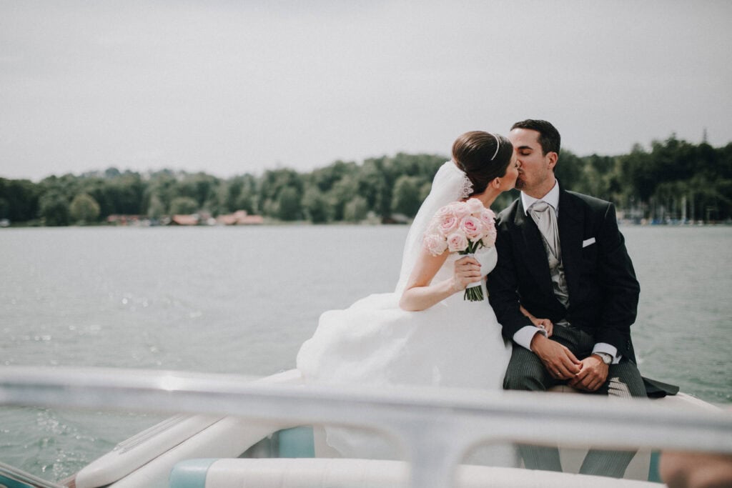 Hochzeitsfoto am Wasser, Braut und Bräutigam küssen auf einem Boot in Tirol.