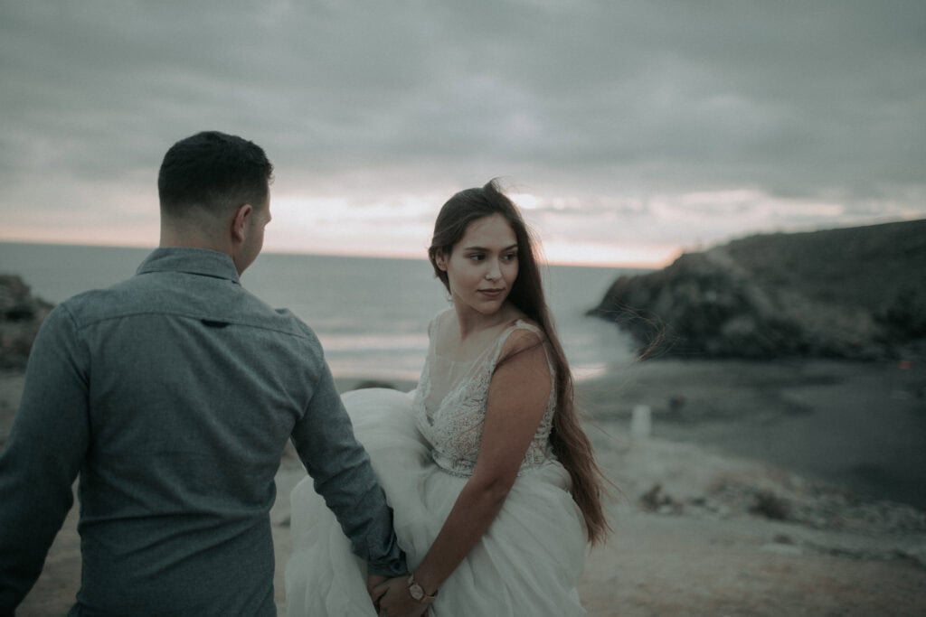 Trauriges Brautpaar am Strand bei Sonnenuntergang, Hochzeitsfotos in Tirol, emotionales Hochzeitsbild, Natürliche Hochzeitsfotografie, internationale Hochzeitsfotografen.