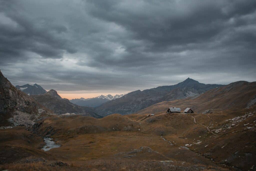 Dunkle Regenwolken über den Alpen, mit einsamen Berghütten und einer Berglandschaft bei Sonnenuntergang in Tirol.