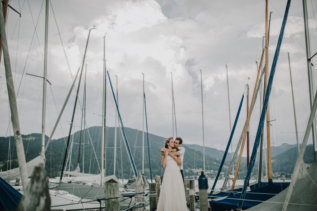 Schöne Hochzeitsfotos am Hafen mit Segelbooten und Bergen im Hintergrund.