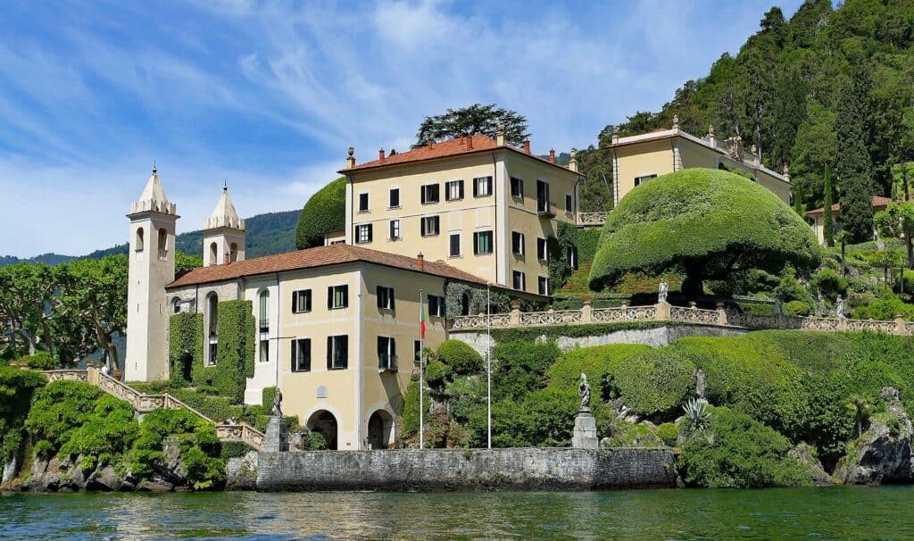 Elegantes Haus am Gardasee in Italien unter blauen Himmel mit grünen Hügeln im Hintergrund.