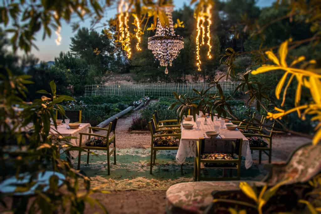 Stimmungsvolle Hochzeitsdinner im Garten bei Sonnenuntergang mit Lichterketten und Kristalllüster.