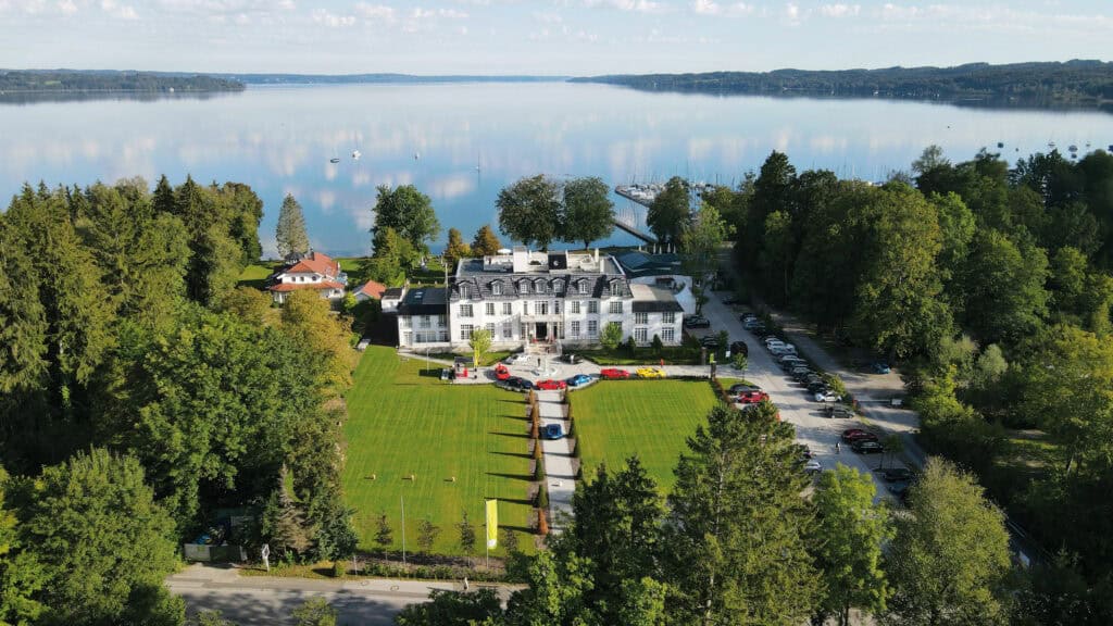 Atemberaubendes Luftbild eines eleganten Schlosses am Ufer eines Sees in Tirol, umgeben von grünen Wäldern.