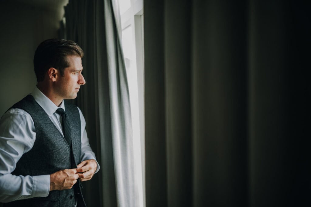 Bräutigam im grauen Anzug blickt aus dem Fenster. 