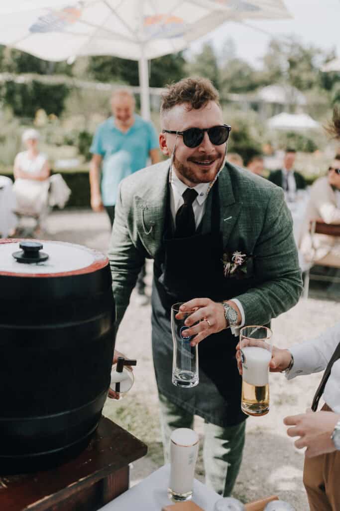 Bräutigam zapft Bier auf Hochzeit in München. Hochzeitsfotograf München.