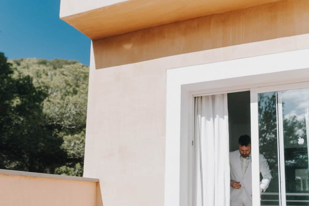 Bräutigam im weißen Anzug am Fenster, Ibiza. Vorbereitung für die Hochzeit. 