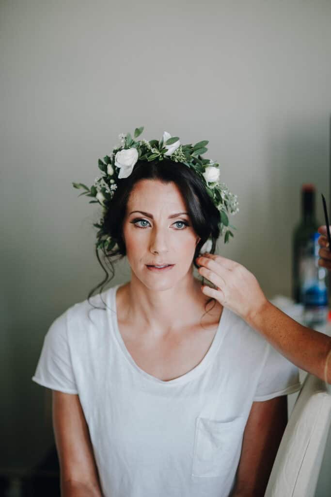 Braut mit Blumenkranz bekommt Frisur.