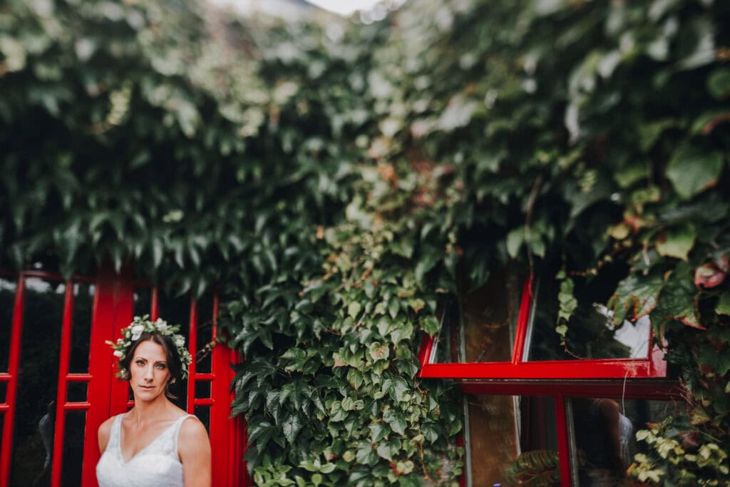 Braut mit Blumenkranz vor roter Tür und Efeu. Hochzeitsfotograf Irland.