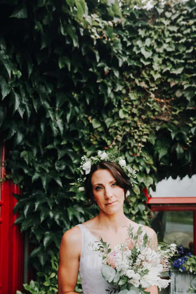 Braut mit Blumenkranz und Strauß vor grün bewachsener Wand. Hochzeitsfotograf Irland.
