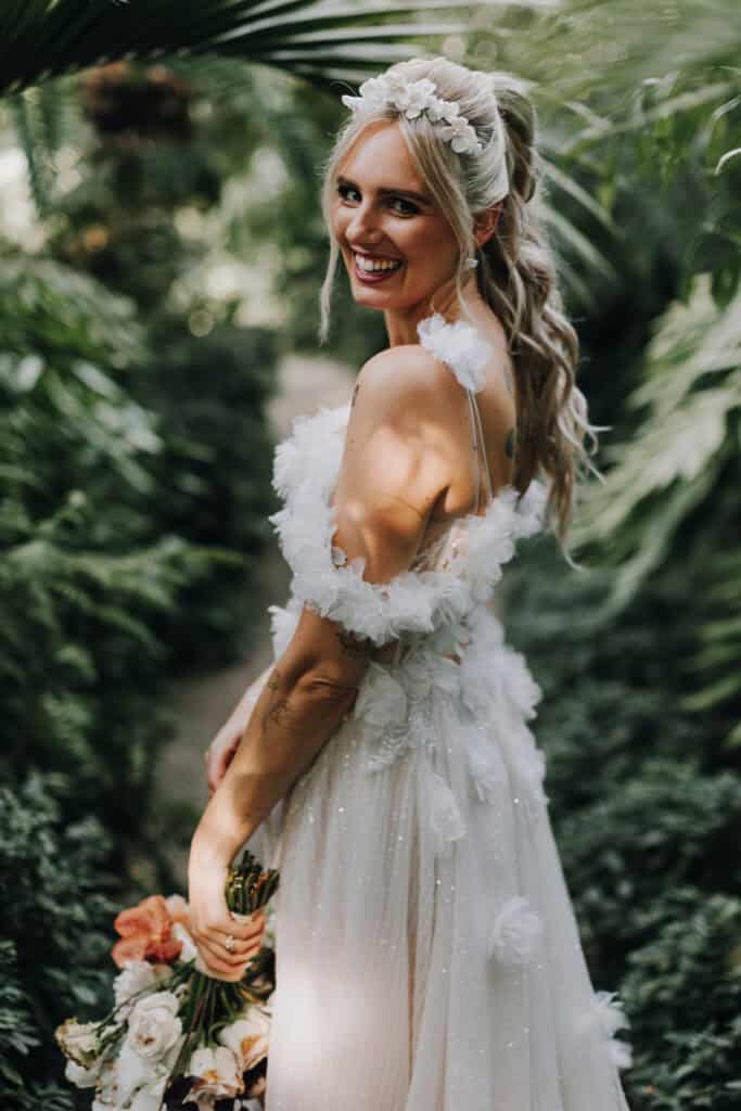 Strahlende Braut im Brautkleid mit Blumen, lächelnd in die Kamera. Hochzeitsfotograf München.