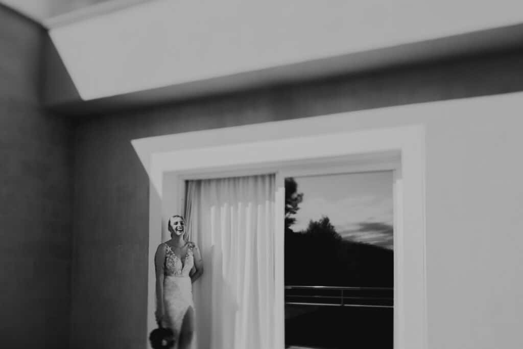 Lachende Braut im Brautkleid vor dem Fenster. 