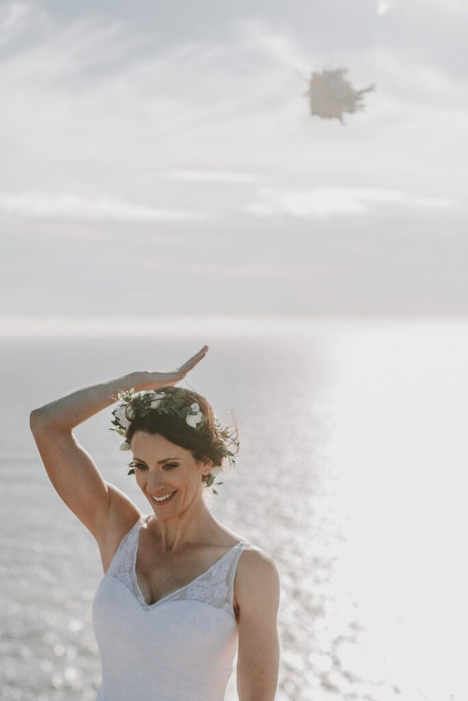Braut wirft Brautstrauß am Meer mit Blumenkranz. Hochzeitsfotograf Irland.