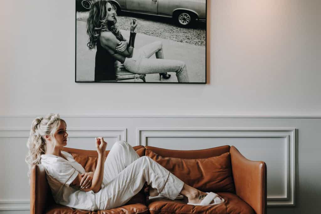 Braut entspannt auf Ledercouch vor Schwarz-Weiß-Foto. Hochzeitstag in München.