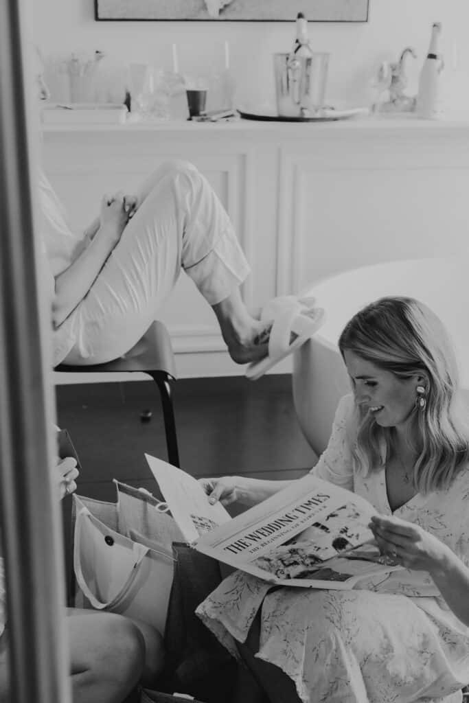 Braut liest "The Wedding Times" mit Brautjungfern vor der Hochzeit. Hochzeitsfotograf München.