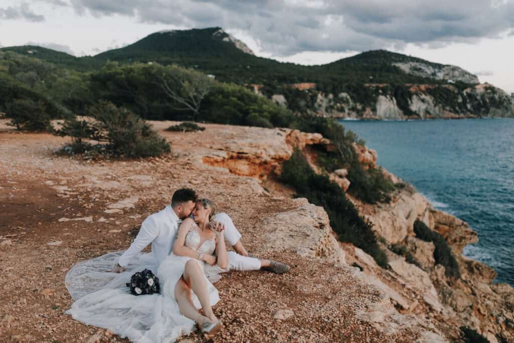 Brautpaar kuschelt auf Felsen mit Meerblick, Ibiza. Hochzeit im Freien. Hochzeitsfotograf Ibiza