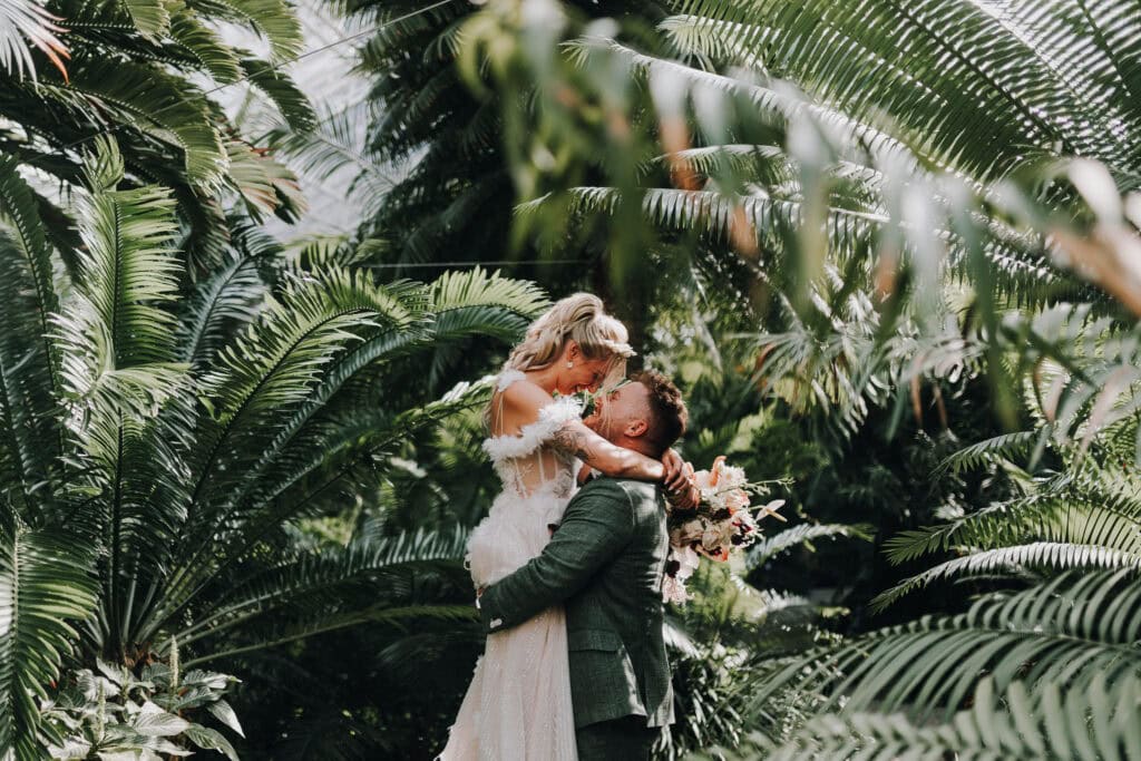Brautpaar in den Armen, umgeben von üppigem Grün. Glücklicher Moment. Hochzeitsfotograf München.