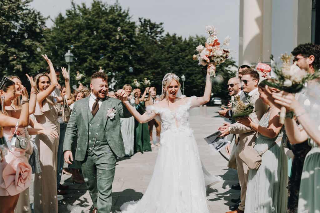 Brautpaar verlässt Kirche, umgeben von jubelnden Gästen und Seifenblasen. München Hochzeitsfotograf.