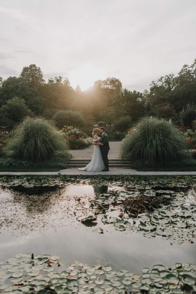 Brautpaar küsst sich im Park bei Sonnenuntergang. Romantische Hochzeit in München.