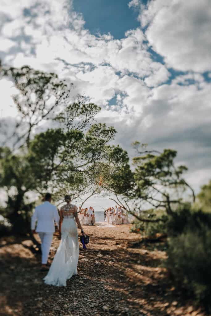 Brautpaar geht zur Strandhochzeit auf Ibiza. Der Himmel ist bewölkt. Hochzeitsfotograf Ibiza.