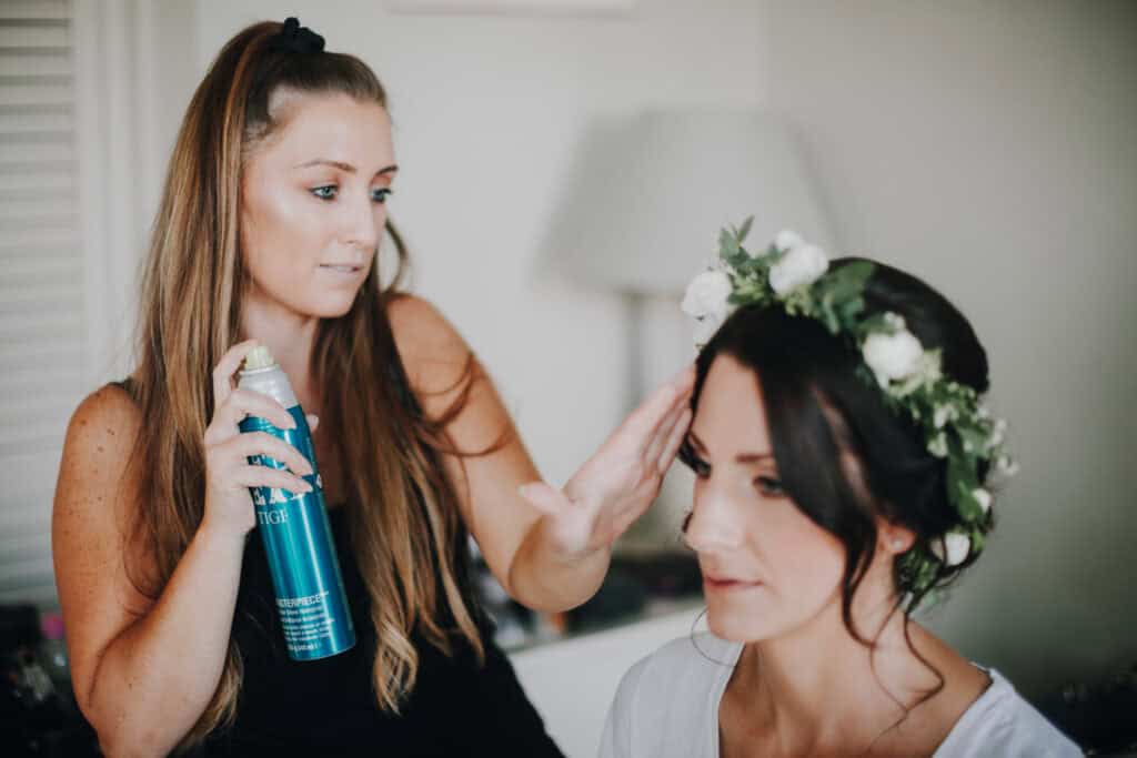 Brautstyling: Friseur sprüht Haarspray auf Braut mit Blumenkranz.