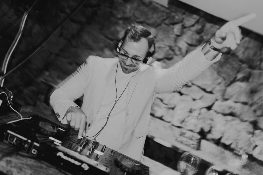 DJ legt auf, Ibiza Hochzeit. Mann mit Kopfhörern und weißem Sakko am DJ-Pult.