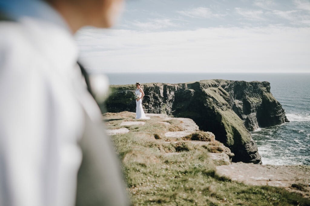 Braut auf Klippen in Irland mit Bräutigam im Vordergrund. Hochzeitsfotograf Irland.