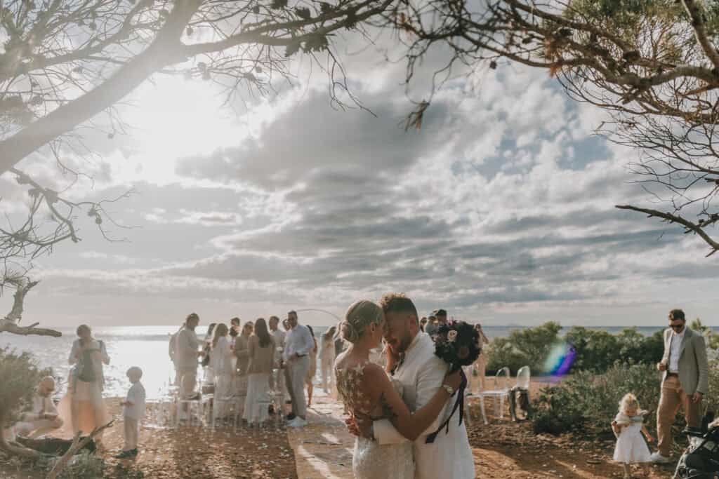 Brautpaar umarmt sich bei Hochzeit auf Ibiza. Zeremonie im Freien mit Gästen.