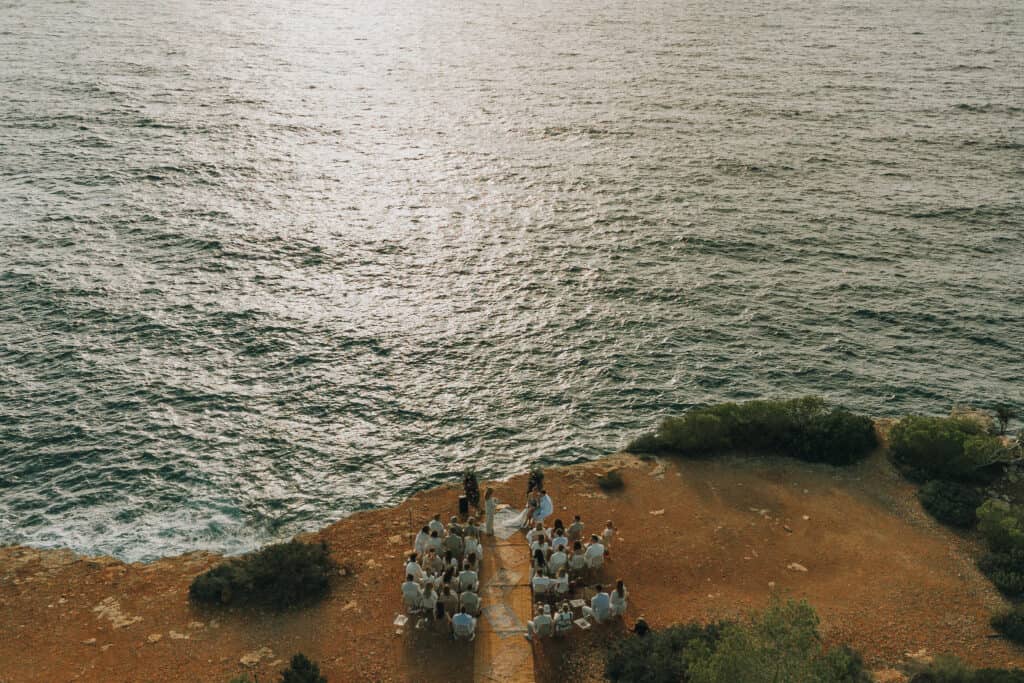 Hochzeitszeremonie auf Ibiza Klippe mit Meerblick. Brautpaar und Gäste in Weiß.