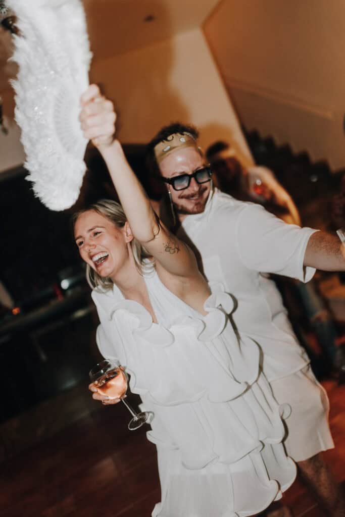 Fröhliche Frau mit Fächer tanzt mit Mann auf Party. Hochzeit Ibiza?