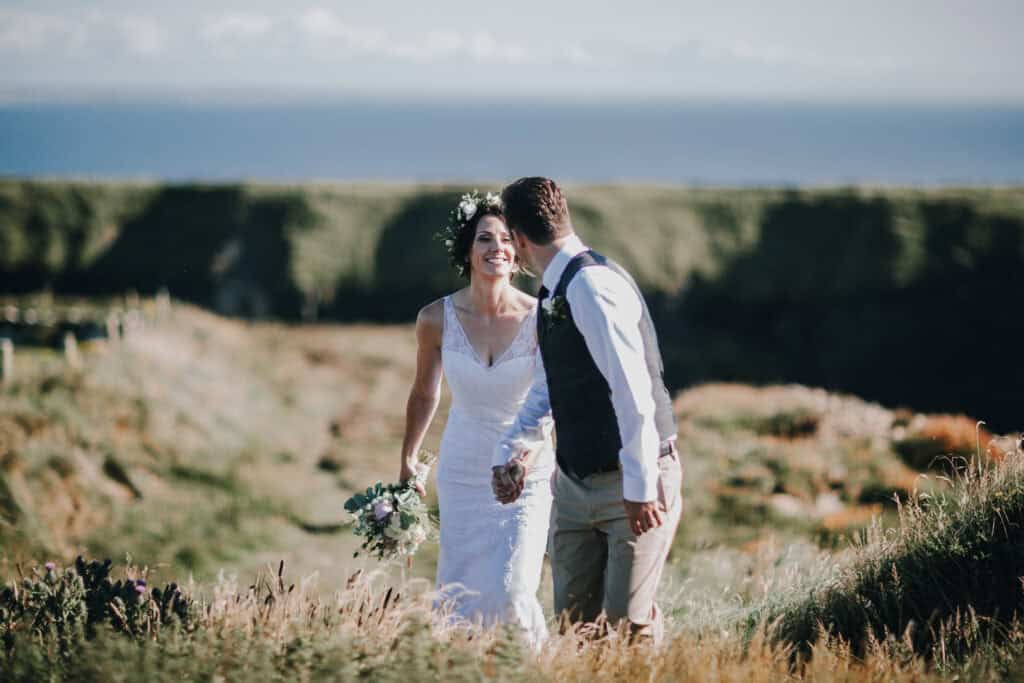 Lächelnde Braut mit Bräutigam in Irland. Blumenkranz, Brautstrauß, Küssender Mann. Hochzeitsfotograf Irland.