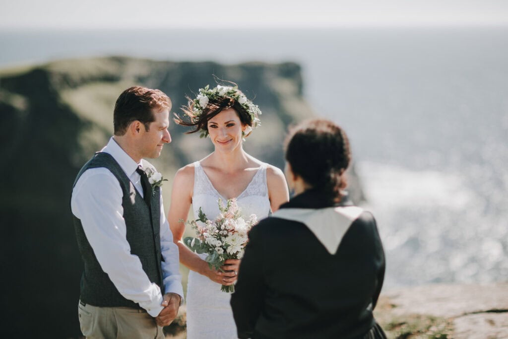 Brautpaar bei irischer Klippenhochzeit mit Blumenkranz und Blick aufs Meer.