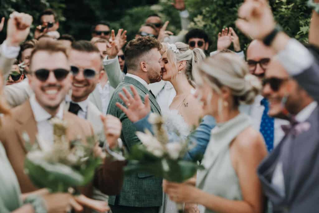 Brautpaar küsst sich inmitten jubelnder Hochzeitsgäste. Fröhliche Hochzeit in München.