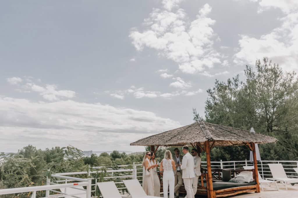 Hochzeitsgesellschaft unter Strohdach auf Ibiza mit Blick auf die Landschaft.