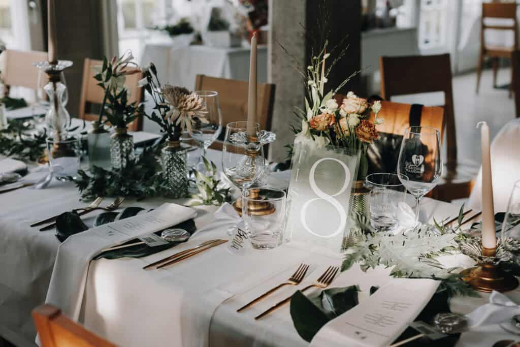 Hochzeitstafel mit Blumenschmuck, Kerzen, goldenem Besteck und Tischnummer 8. Elegante Hochzeitsdekoration in München.