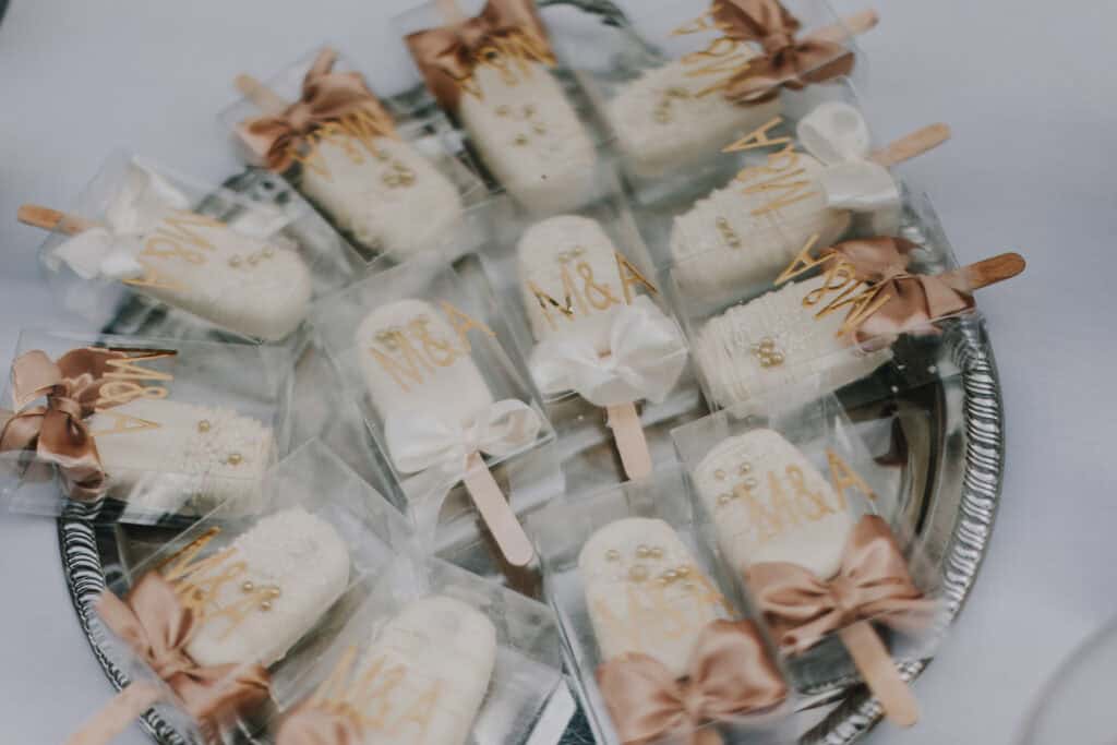 Verpackte Hochzeitstorte-Pops mit Schleifen und Initialen "M&A" auf einem silbernen Tablett.