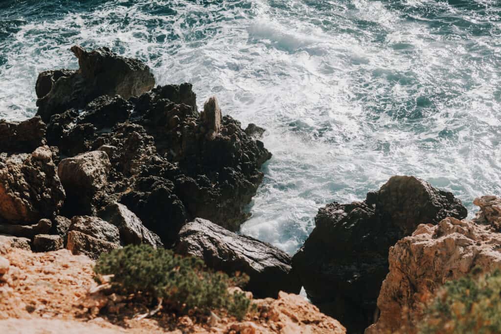 Küstenfelsen auf Ibiza mit Gischt und türkisfarbenem Meer. Rau und natürlich.