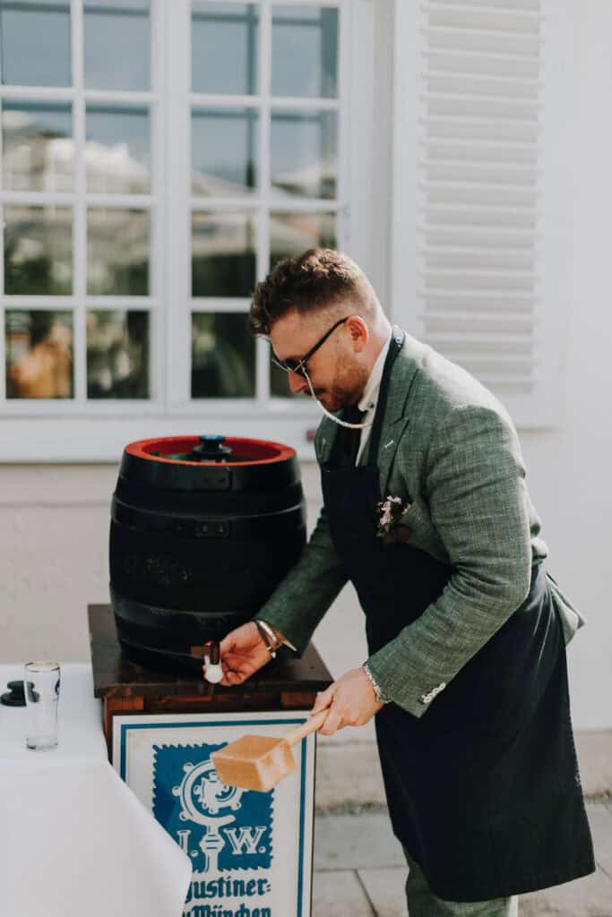 Mann zapft Bierfass an. "Löwenbräu Justiner-München" ist sichtbar.