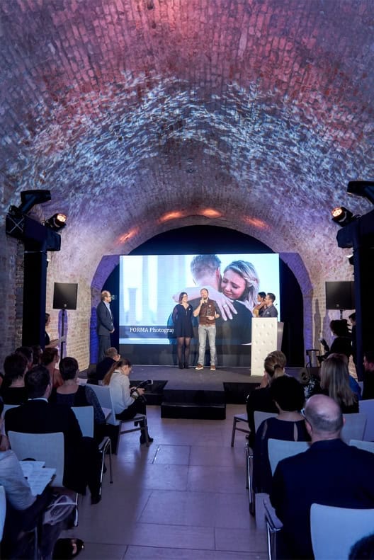 Präsentation mit zwei Personen auf Bühne vor Publikum in Gewölbekeller. Leinwand mit Foto im Hintergrund.