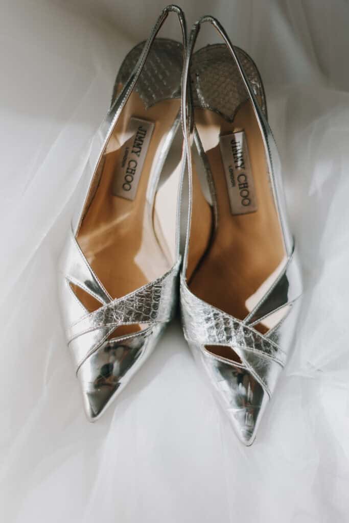 Silberne Jimmy Choo Brautschuhe auf weißem Tüll. Luxuriöse Hochzeitsschuhe für die Braut. Jimmy Choo London Logo sichtbar.